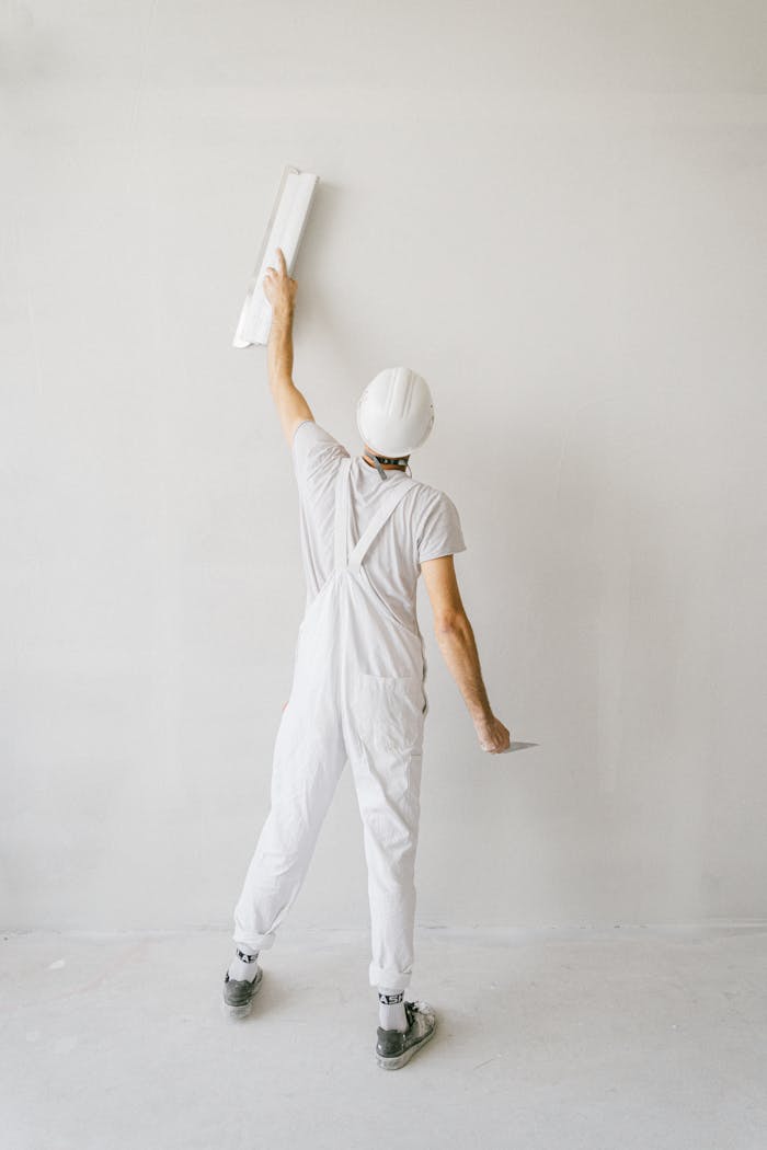 Back view of construction worker in overalls painting a wall white.